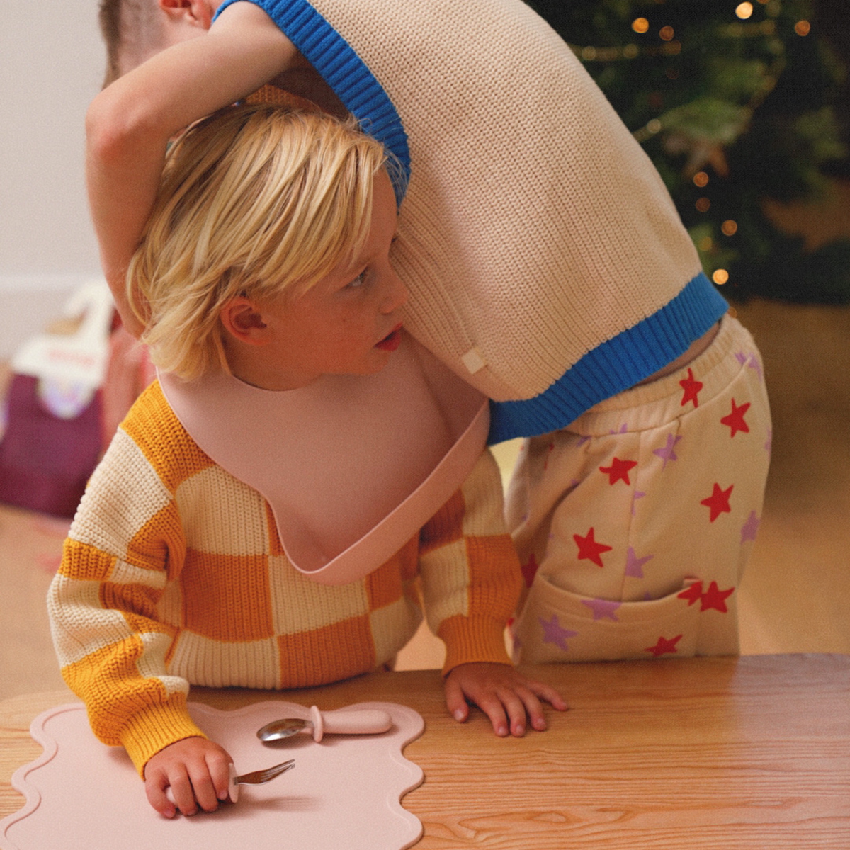 Two children playing at a table wearing baby bibs designed by Rommer