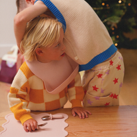 Two children playing at a table wearing baby bibs designed by Rommer