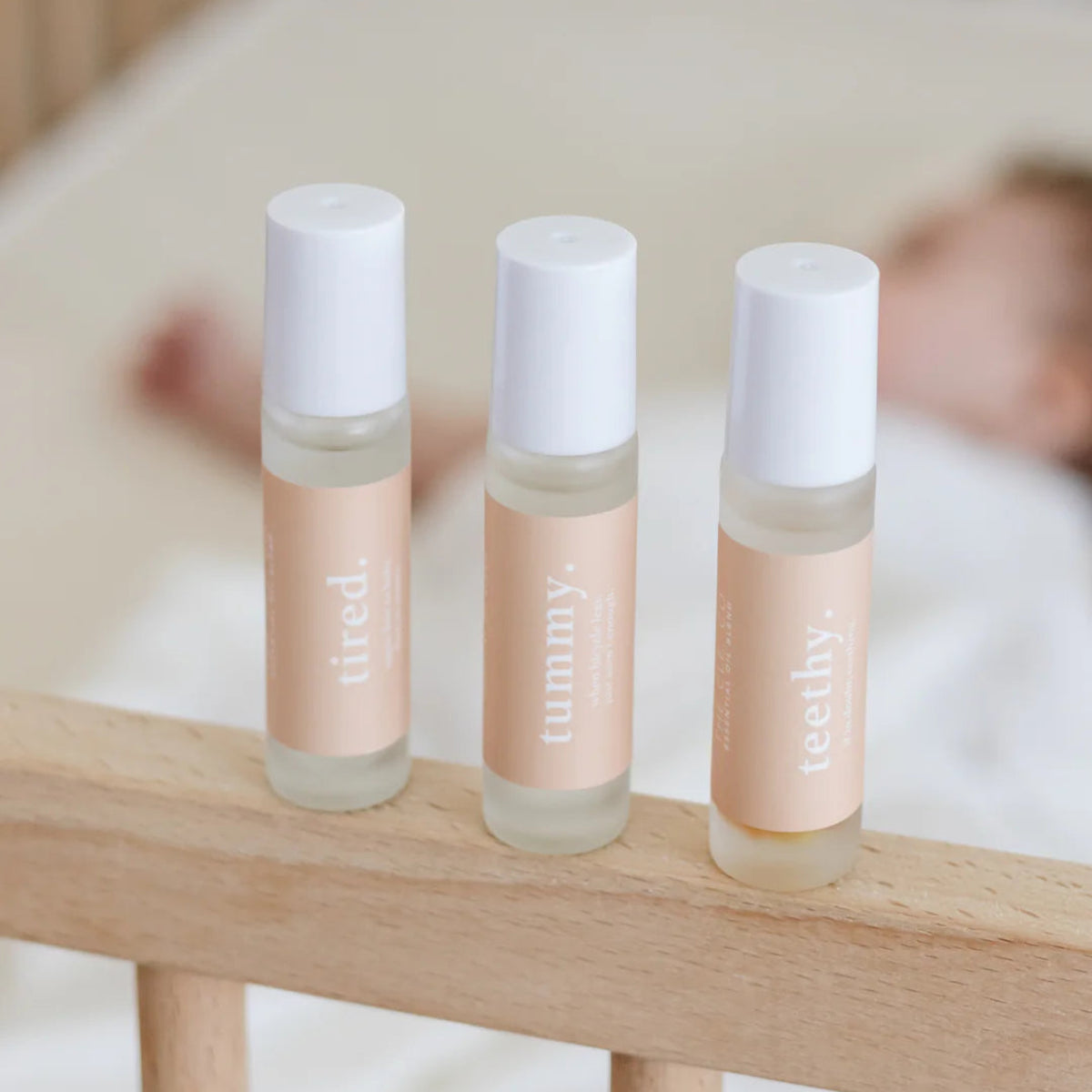 Roll-on essential oils for babies labelled tummy, teethy and tired, with a blurred baby in the background.