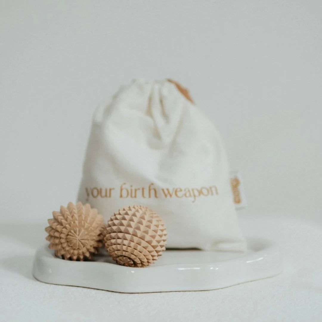 Two textured birth weapon acupressure balls on a white stand with a drawstring bag labelled 'your birth weapon' in the background.