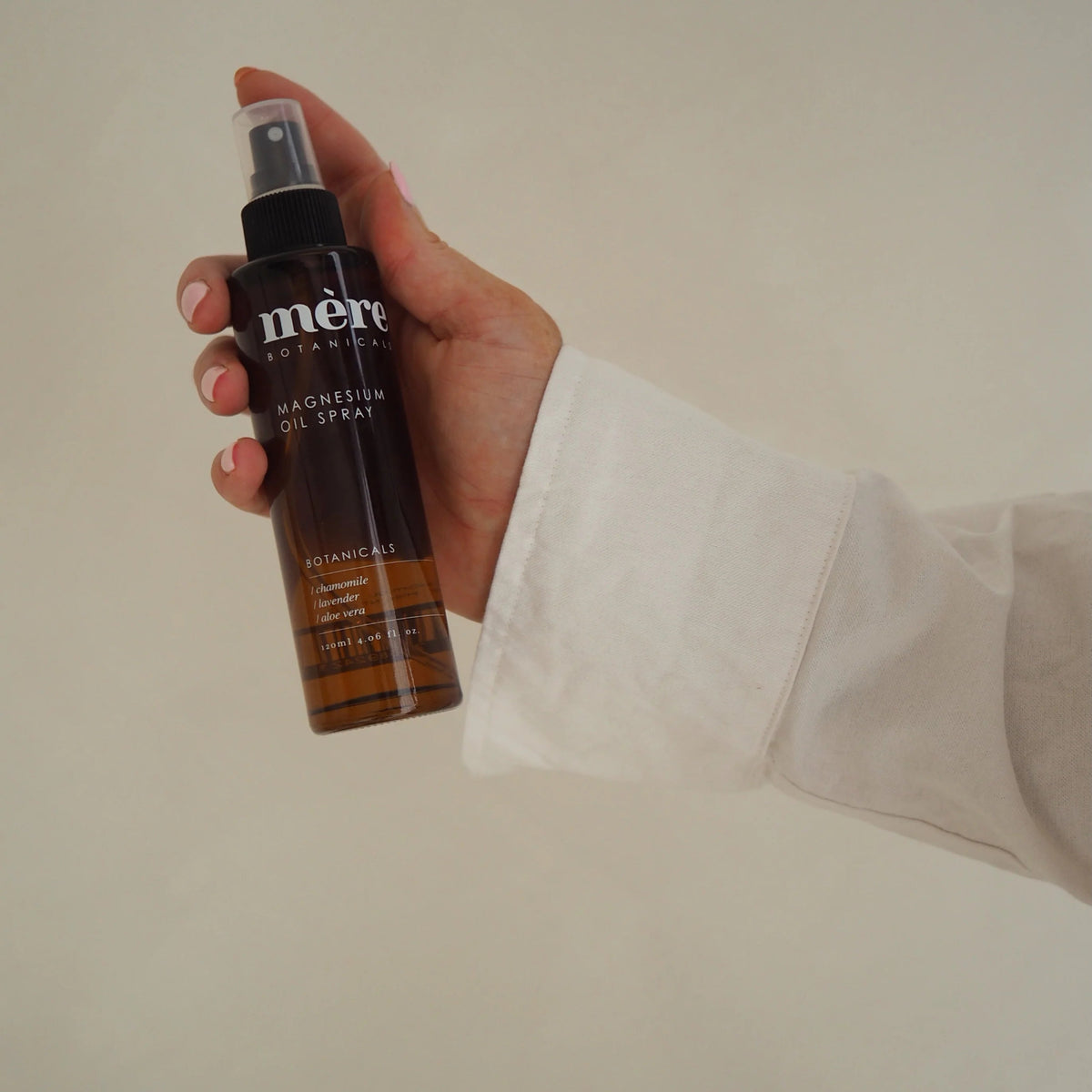 Hand holding a bottle of Mere Botanicals magnesium spray against a plain background