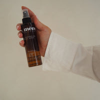 Hand holding a bottle of Mere Botanicals magnesium spray against a plain background
