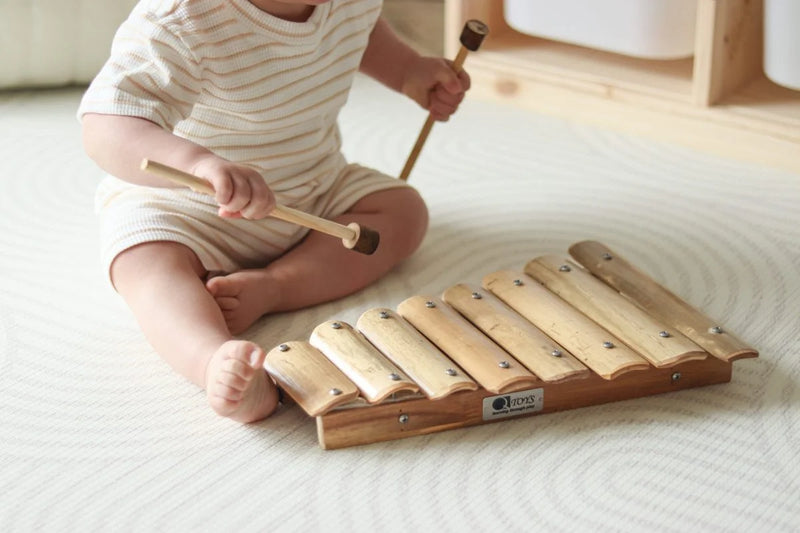 Child playing with a wooden xylophone on a light-colored floor.