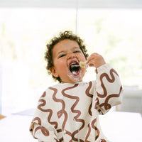 Child eating a yogurt with Rommer kids cutlery wearing a patterned rommer smock bib