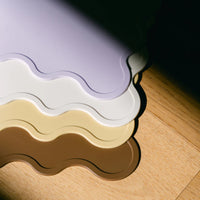 Stack of Rommer silicone placemats in purple, white, yellow and brown on a wooden benchtop