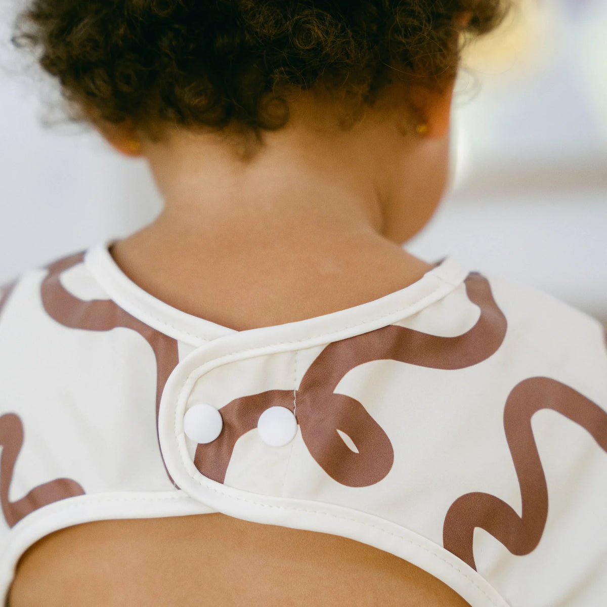 Close-up of a child wearing a Rommer smock bib with brown patterns on a blurred background