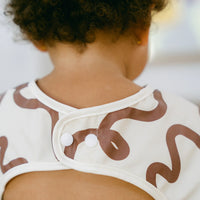 Close-up of a child wearing a Rommer smock bib with brown patterns on a blurred background