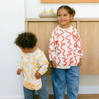 Two children wearing colourful smock bibs designed by Rommer standing in a kitchen.